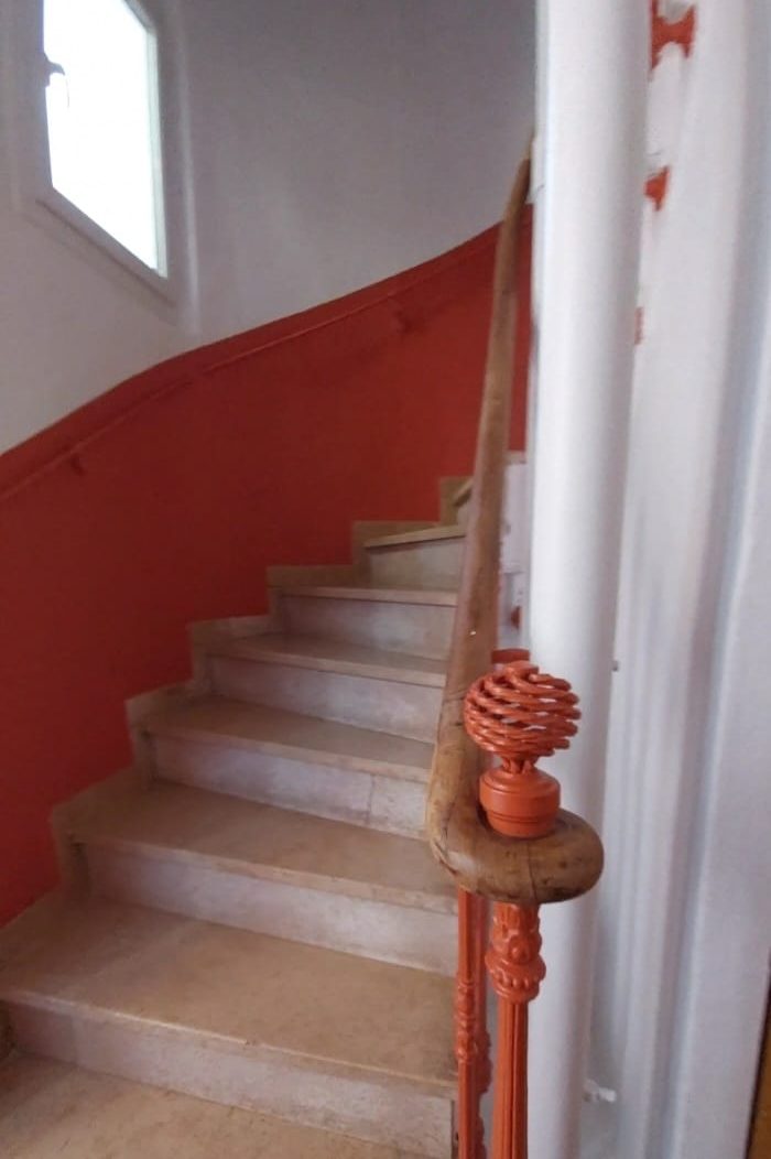 Après travaux : escalier tournant au mur repeint en terracotta et rampe en fer forgé assortie