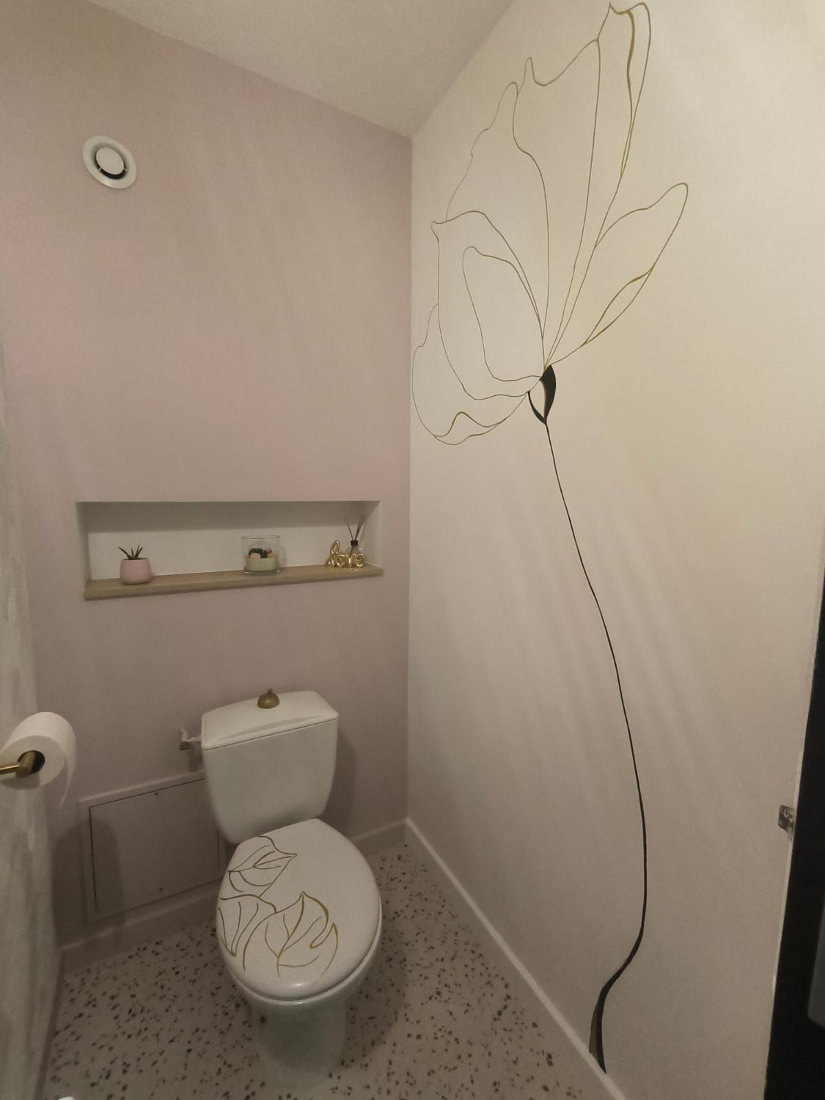 Toilettes aux murs rose poudré, avec une grande fleur peinte au trait sur le mur