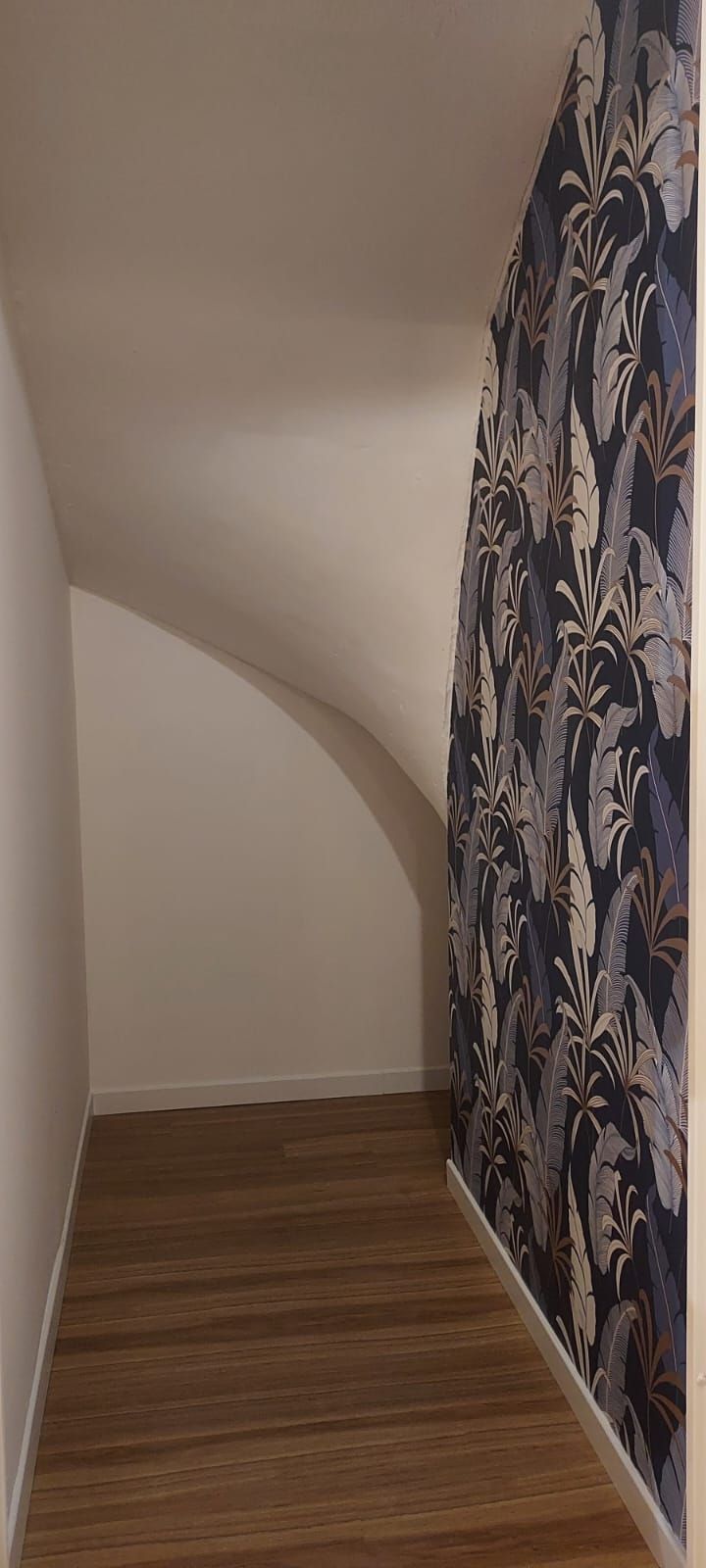 Dessous d'escalier aménagé, avec un mur en papier peint à motifs végétaux sur fond bleu nuit